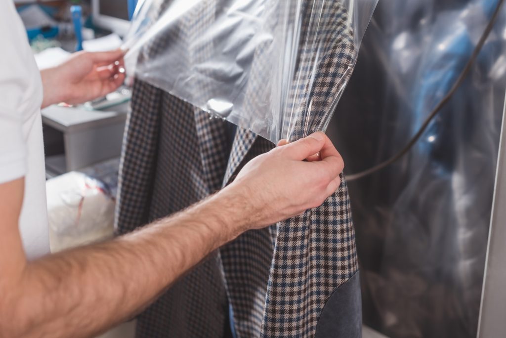 cropped shot of dry cleaning worker packing jacket in plastic bag